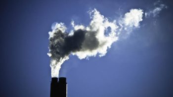 Cheminée d'usine dégageant une large fumée grise devant un ciel bleu