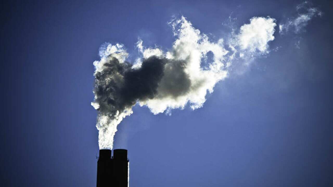 Cheminée dégageant un large panache de fumée grise devant un ciel bleu