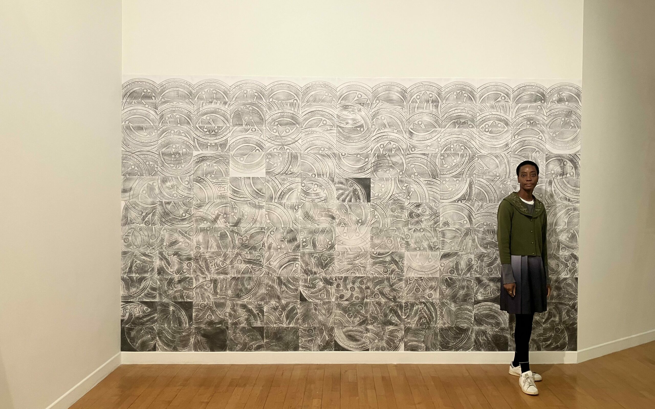 Tanoé Ackah devant sa fresque Car le Marigot va à la rivière. Les feuilles ont été réalisés une par une avec de la mine de plomb. L’assemblage des 143 feuilles a ainsi donné l’œuvre.